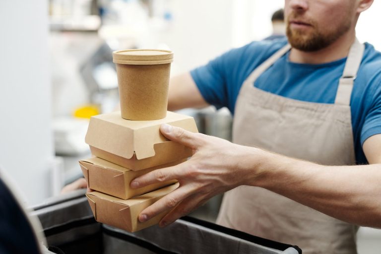 A person holds a stack of delivery food items in a restaurant.