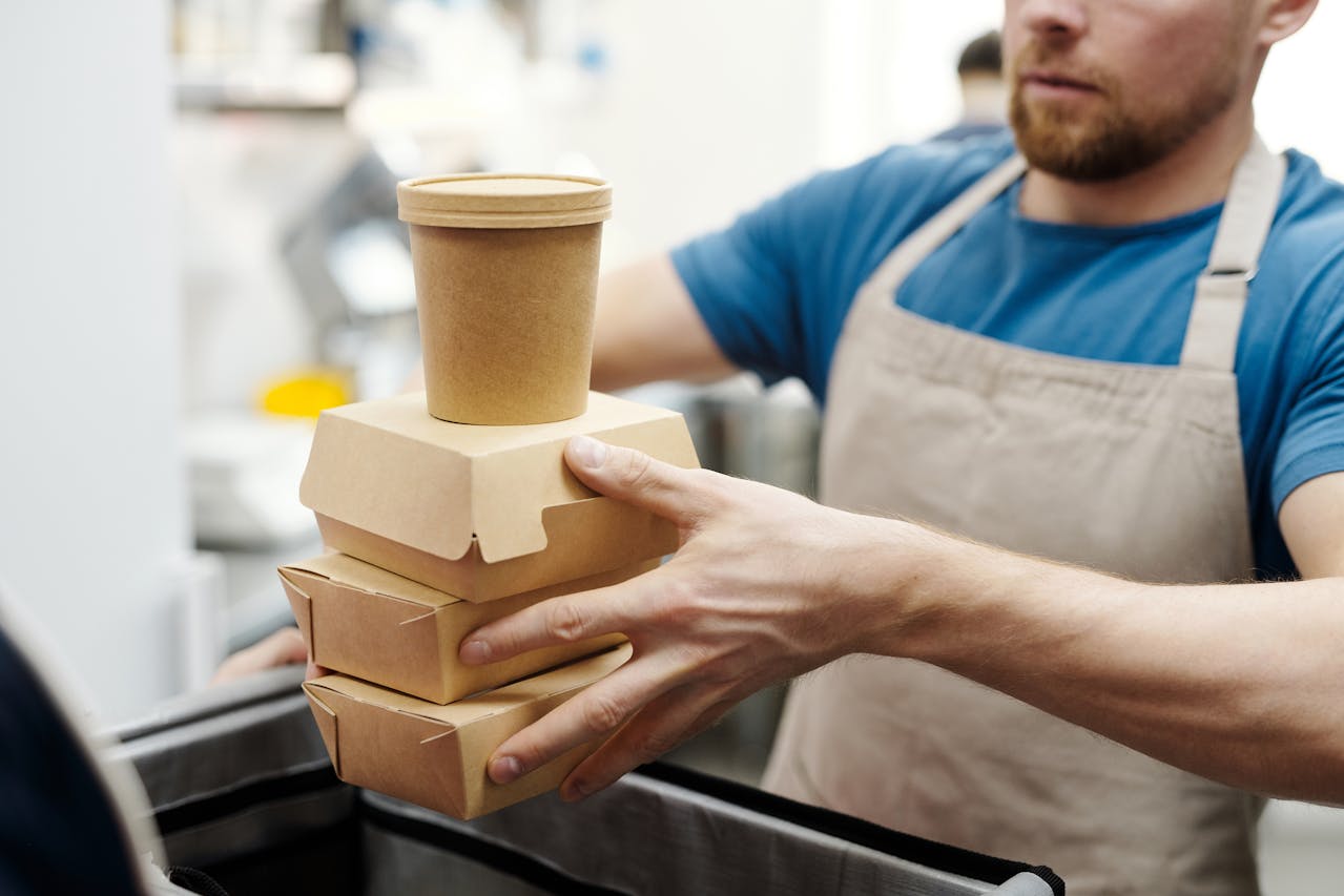 A person holds a stack of delivery food items in a restaurant.