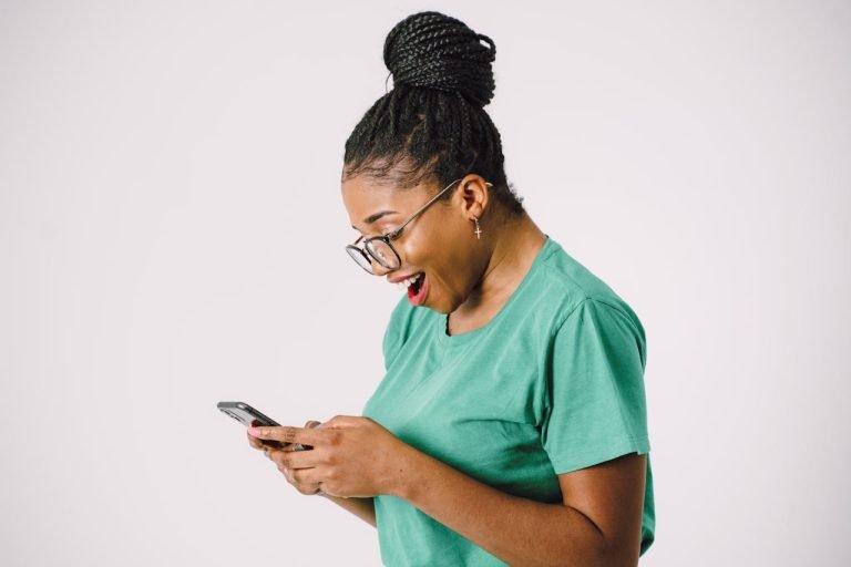 A woman in scrubs smiles and looks at her phone.